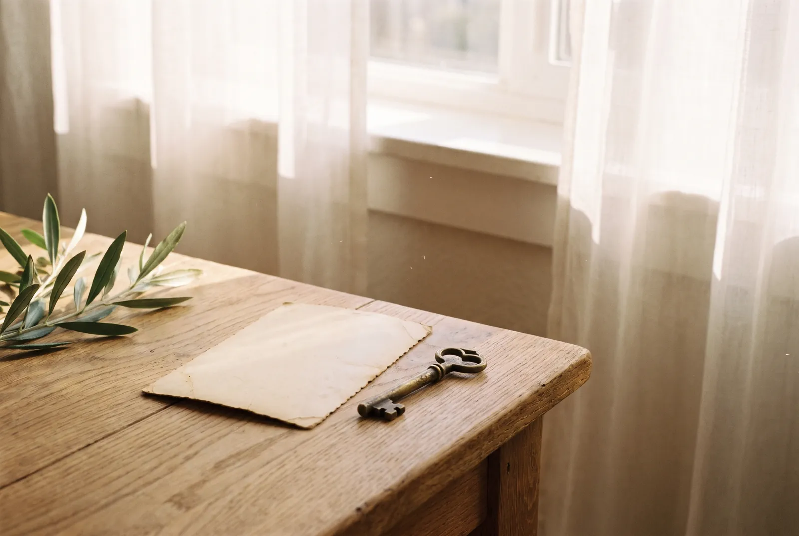 Una foto antigua boca abajo sobre una mesa de madera clara, junto a una llave y una rama de olivo